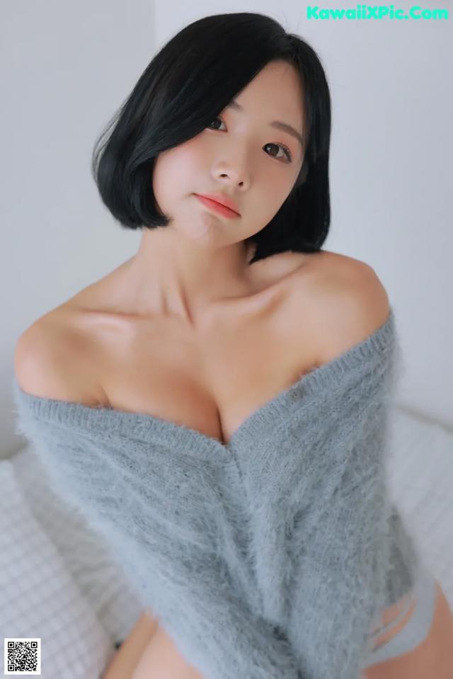 A woman in a gray sweater is posing on a bed.