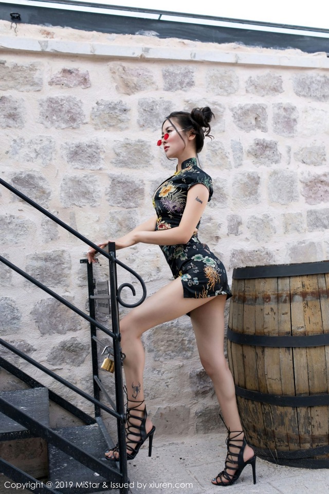 A woman in a black dress standing next to a wooden barrel.