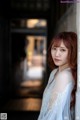 A woman with long red hair leaning against a wall.