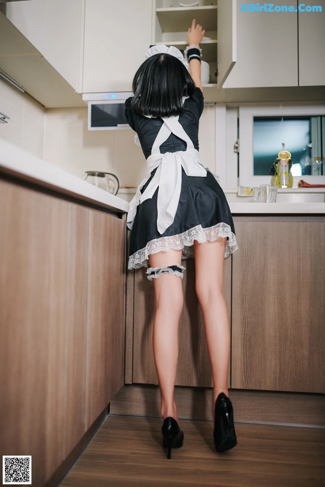 A woman in a maid outfit is standing in a kitchen.