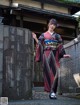 A woman in a kimono standing in front of a gate.