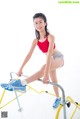 A woman in a red top and gray shorts is doing a squat on a bar.