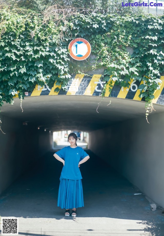 A woman in a blue dress standing in a tunnel.